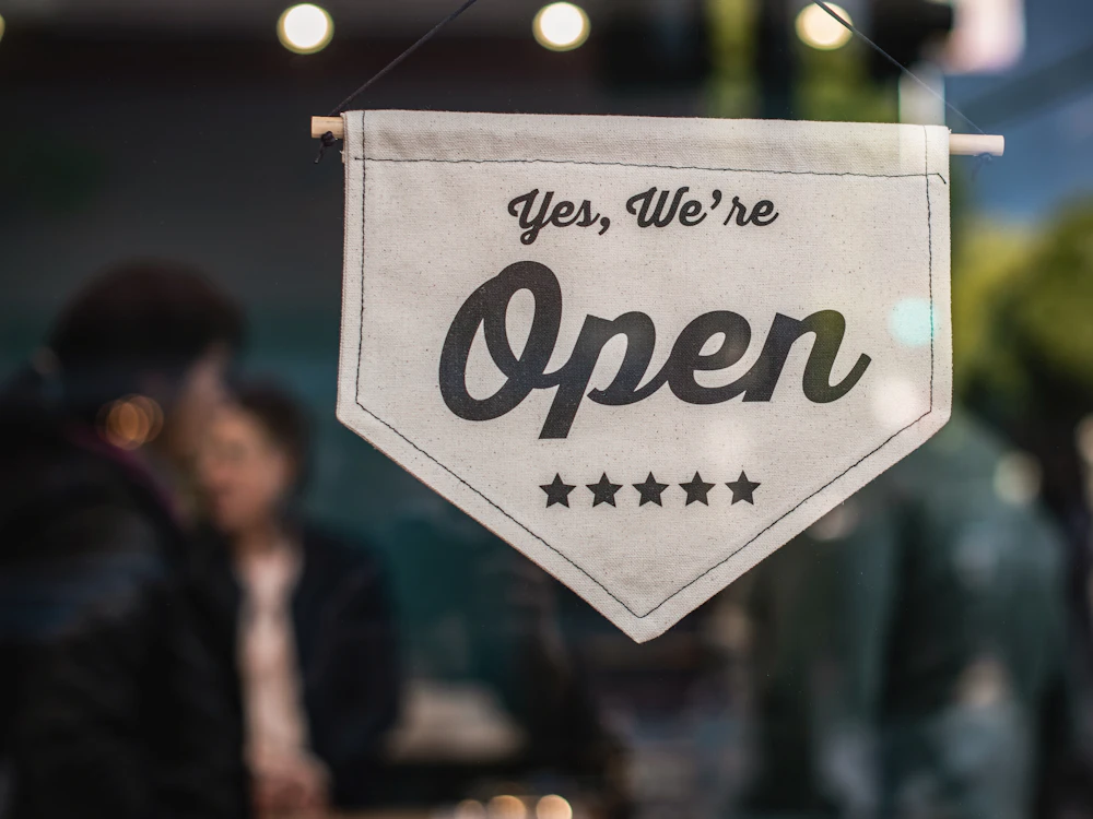 A canvas sign reading 'Yes, we're open' with five stars hanging in a shop window